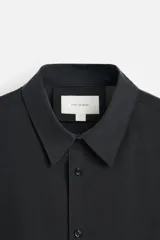 Camisa negra relaxed fit confeccionada en tejido fluido con mezcla de viscosa. Tiene cuello solapa, manga larga con puño abotonado y cierre frontal con botones.