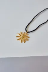 Collar con dije de acero quirúrgico hipoalergénico con forma de flor o sol estilizado, unido a un tiento trenzado negro.