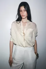 Camisa de manga larga con cuello solapa, a rayas verticales grises y blancas. Tiene un bolsillo de plastrón en el delantero y cierre frontal con botones.