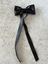 Moña de cuero color marrón con forma de lazo y tiras colgantes.