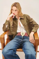 Campera verde militar de algodón, de corte recto, con cuello camisero, cierre frontal con botones a presión, bolsillos plaqué con solapa y bordado a tono en la espalda.