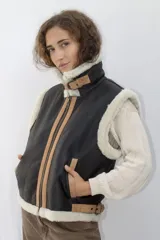 Chaleco negro de cuero con cuello y borde inferior de piel sintética negra. Cierre frontal con cremallera color cobre y detalles en cuero color tostado.