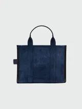 Bolso tote mediano Marc Jacobs The Suede Leather Blocked, color azul marino, confeccionado en gamuza con detalles y asas en cuero liso negro. Presenta un compartimento principal con cierre superior y correa ajustable y desmontable para llevar al hombro o cruzado.