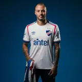 Camiseta de fútbol Umbro del Club Nacional de Football, modelo Home 2025. Diseño blanco con detalles en azul y rojo en cuello y mangas. Incluye logo de Umbro, escudo del club y sponsor Antel en el frente.