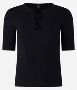 Blusa blanca de mangas cortas, confeccionada en Rib, con cuello redondo y lazos de terciopelo negros uniendo la abertura en la parte de abajo.