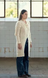 Cárdigan largo color crudo tejido a crochet en lana merino, con cuello en V, cierre frontal con botones de guampa tallados a mano, mangas largas con trenzas 3D y puños extra largos.