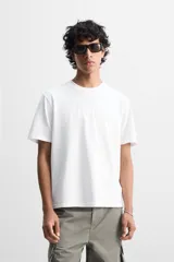 Camiseta blanca de algodón de peso medio, corte slim fit, cuello redondo y manga corta.