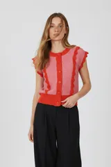 Chaleco sin mangas de acrílico, color rosa con detalles de volados en naranja. Tiene cuello redondo y cierre frontal con botones.