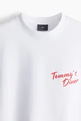 Remera blanca de corte oversized con estampado rojo de la leyenda "Tommy's Diner" en el pecho.