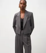 Blazer corto de sastrería color gris oscuro, con solapas estructuradas, manga larga y corte ajustado. Se combina con un top de encaje negro y pantalón ancho a juego.