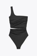 Traje de baño de dos piezas negro, con corpiño asimétrico de un solo hombro con hebilla metálica en el tirante, detalle cut out en el delantero y frunces laterales. La parte inferior es de tiro alto con frunces laterales.