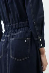 Vestido camisero de jean azul oscuro, corte evasé, largo midi, con cuello camisero, cierre frontal con botones, mangas largas con puños abotonados, bolsillos en el pecho y tajo lateral.