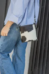 Cartera tipo bucket de cuero con estampado animal print de vaca en blanco y negro. Tiene correa larga de cuero negra regulable y removible.