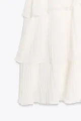 Minivestido blanco con cuello halter ajustable con lazos y falda escalonada con volantes. Espalda descubierta.