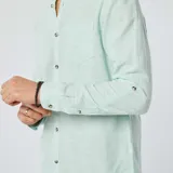 Camisa celeste claro de lino con cuello mao, manga larga con puños abotonados y bolsillo de parche en el pecho.
