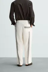 Pantalón de lino color crudo con rayas verticales negras, corte relaxed fit, cintura elástica ajustable con cordón, bolsillos laterales y traseros.