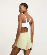 Bermuda deportiva femenina de microfibra color amarillo claro, con diseño de doble capa: un short interno ajustado y una capa externa suelta con bajo redondeado. Posee cintura alta.