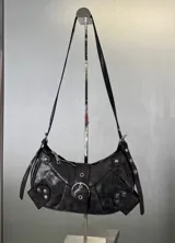 Cartera negra de cuero sintético con correa de hombro ajustable, cierre superior con cremallera y hebilla decorativa en la parte delantera.