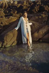 Vestido largo blanco con escote en V profundo y mangas largas acampanadas. Presenta aberturas en la parte delantera y detalles de cordones cruzados en el escote.