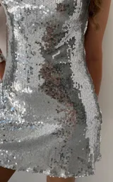 Vestido corto de lentejuelas plateadas con tiras finas regulables y escote halter con abertura en el centro.