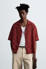 Camisa color ladrillo con estampado de flores en relieve, corte relaxed fit, cuello bowling, manga corta, bajo con aberturas laterales y cierre frontal con botones.