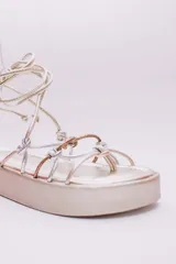 Sandalias de plataforma color dorado con tiras plateadas y cobrizas para atar alrededor del tobillo.