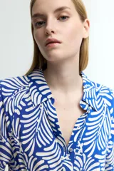 Vestido midi camisero con estampado de hojas blancas sobre fondo azul. Tiene cuello camisero, botonadura frontal, mangas cortas raglán, elástico en la cintura y cinturón extraíble para atar.