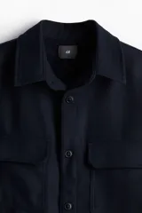 Sobrecamisa azul marino de tejido afieltrado con cuello, botones adelante y canesú en la espalda. Tiene bolsillos superiores con solapa, puños abotonados y bajo redondeado.