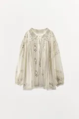 Camisa color crema de algodón con cuello bobo, mangas largas abullonadas y bordados florales con encaje.