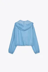 Chaqueta celeste de denim con capucha, cierre frontal con cremallera, bolsillos delanteros y mangas largas con puños elásticos.