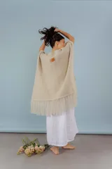 Ruana de lana merino color beige, tejida a mano con detalles de brillos y flecos.