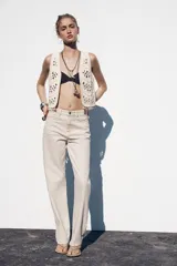 Chaleco abierto de punto color crudo con manga sisa y detalle de conchas en el ruedo.