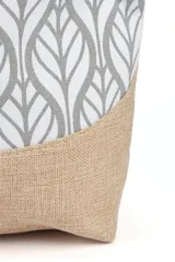 Bolso tipo tote playero con cuerpo estampado en patrón de hojas estilizadas en gris y blanco, y base de arpillera color beige. Las asas son de cuerda gruesa trenzada de color crudo.