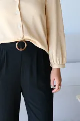 Pantalón negro de tiro alto con pliegues frontales y pierna ancha, ajustado a la cintura con un cinturón marrón claro con hebilla circular.