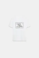 Camiseta blanca de algodón con cuello redondo y mangas cortas. Estampado frontal con texto "Meet me at Palais Lomtam, 7, Passage des Rêveries" enmarcado en un diseño ondulado.