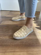 Zapatilla color beige con capellada de cuero entretejido y suela blanca de goma.