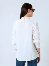 Blusa blanca de mangas largas con cuello alto fruncido y puños elásticos.