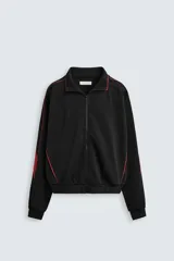 Chaqueta deportiva negra con cuello alto, cierre frontal con cremallera y ribetes rojos en hombros y mangas.