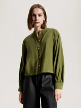 Camisa verde oliva de corte cropped, sin cuello, con cierre frontal de botones y mangas largas abullonadas con puños abotonados.