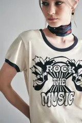 Remera color crema de algodón con cuello y mangas con ribete azul marino. Estampado frontal con la frase "Rock the Music" en letras negras con detalles de estrellas.