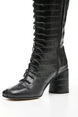Botas altas de cuero negro con textura tipo cocodrilo, caña alta hasta la rodilla, punta cuadrada y cordones frontales.