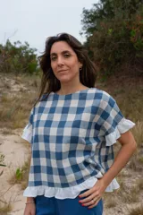 Top de tela a cuadros azul y blanco, con corte cuadrado, mangas cortas con volados y ruedo con volados.
