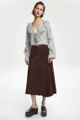 Blusa color marrón con escote en pico, manga larga abullonada con elástico en los puños y volantes en el escote y mangas.