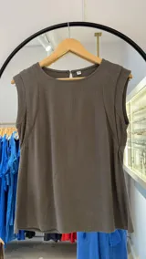 Musculosa color verde seco, con cuello redondo y hombros con detalle de pliegues o frunces que simulan una pequeña manga. Presenta un corte holgado y un pequeño cierre con botón en la espalda.