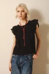 Remera negra sin mangas con volados en los hombros y escote en V. Incluye un collar largo de cuentas con un nudo decorativo. Jeans de tiro bajo.