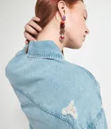 Chaqueta cropped de jean celeste, con cuello con solapa, mangas largas, bolsillos frontales, terminación gastada y cierre frontal con botones.
