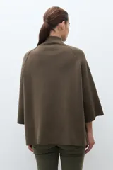 Chaqueta tejida de punto color verde oliva, con cuello alto y cierre frontal de botones a presión. Presenta bolsillos delanteros aplicados y mangas amplias de largo tres cuartos.