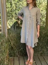 Vestido camisero blanco de lino, con cuello camisero, manga larga con botón para recoger, cierre frontal con botones de nácar, bolsillo en el pecho y diseño asimétrico más largo en la parte trasera.