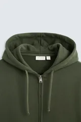 Sudadera negra relaxed fit confeccionada en tejido de algodón compacto con interior en rizo. Cuello con capucha ajustable y manga larga. Bolsillos frontales tipo canguro. Acabados en rib. Cierre frontal con cremallera.