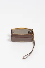 Monedero pequeño de estructura rígida, color negro, con cierre de cremallera y tirador de tejido amarillo mostaza. Presenta un bolsillo exterior frontal y el logo de la marca grabado en dorado.